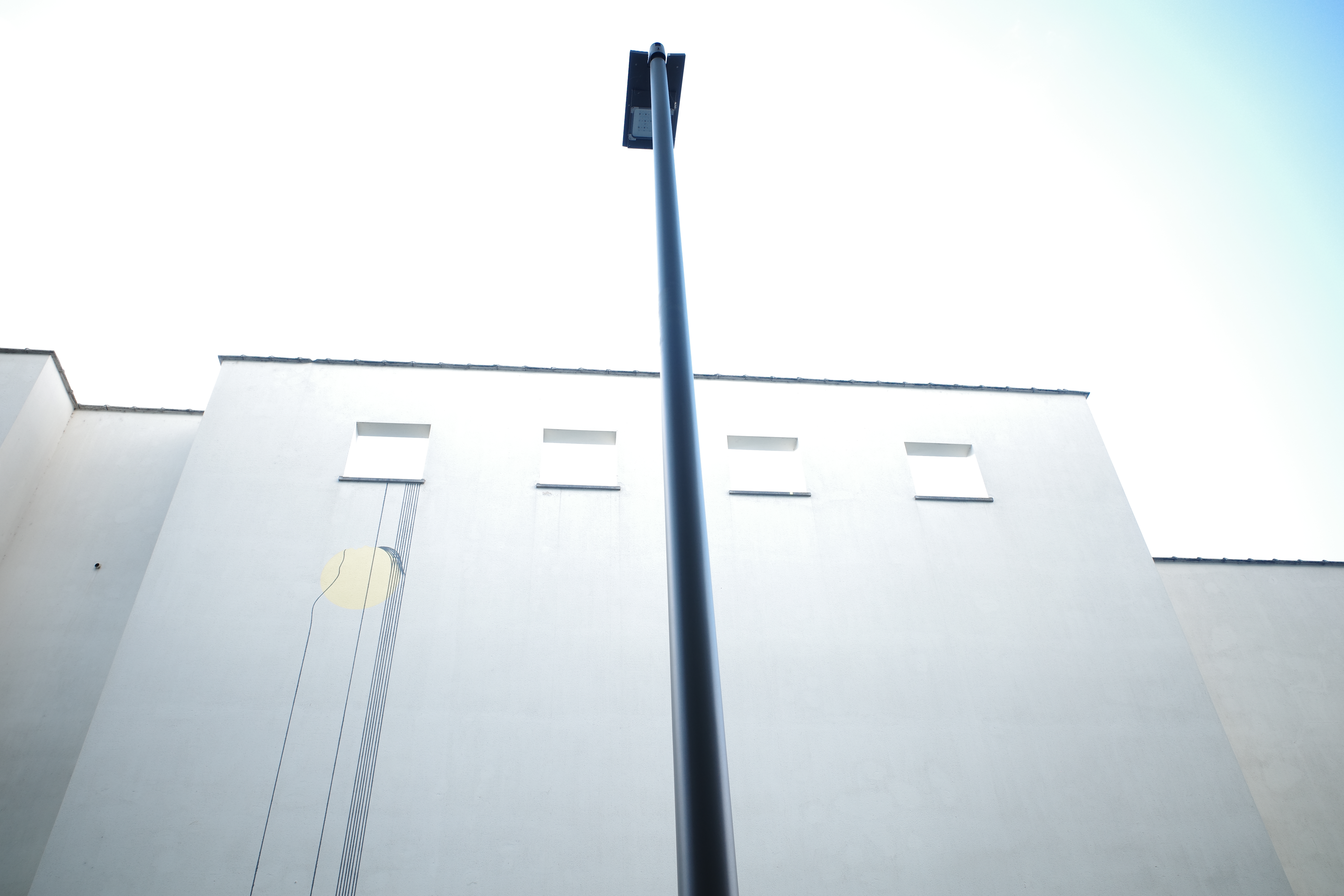 A streetlight rising above a white building beneath a pale blue sky